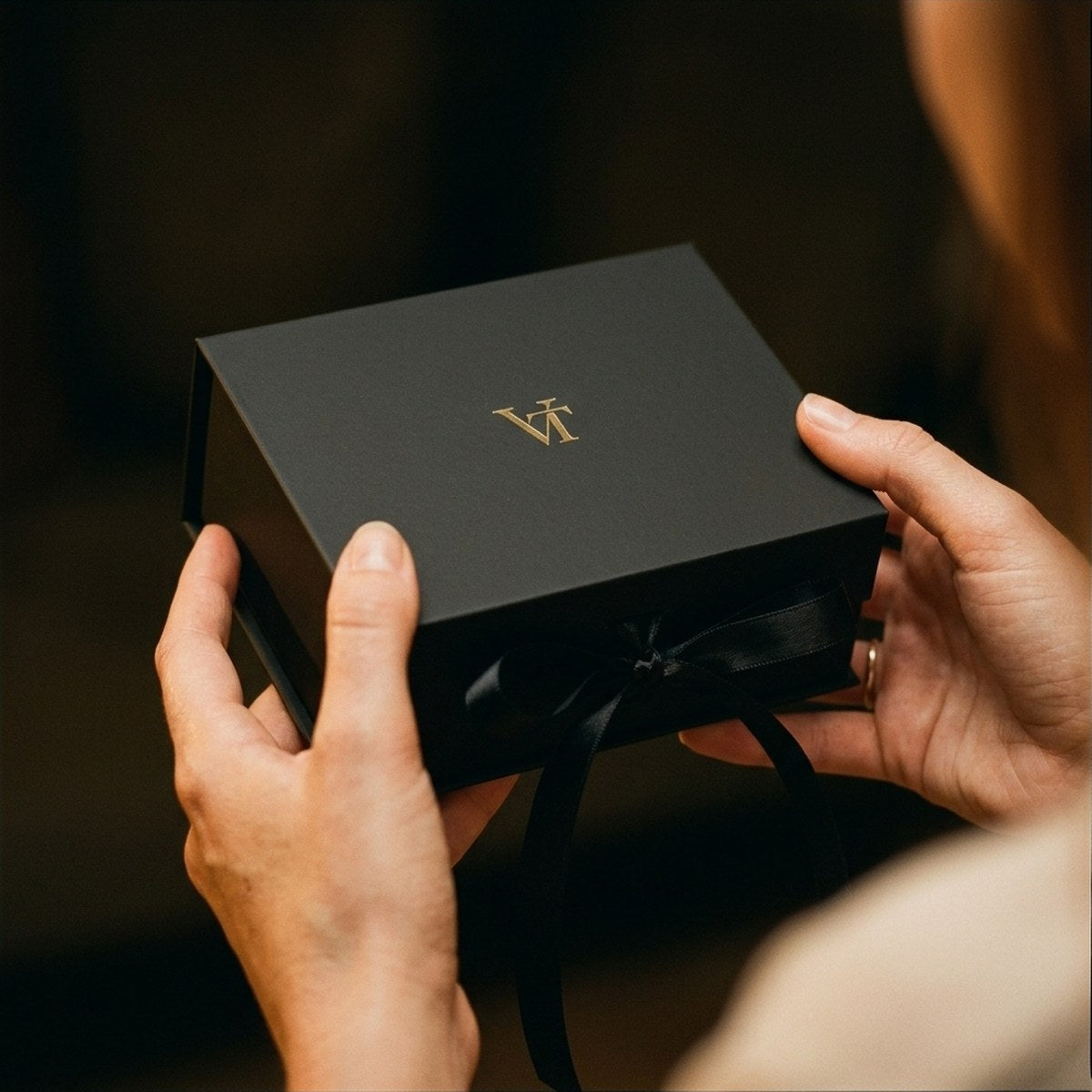 Zwei Hände halten eine schwarze VT Geschenkbox mit Satinband im Auto.