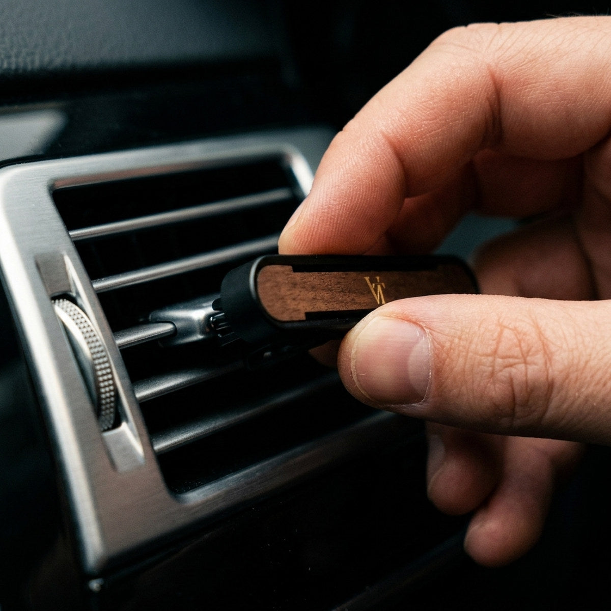 Finger klemmen den VT Autoparfum Clip an eine Lamelle des Lüftungsgitters, die Klammer ist sichtbar
