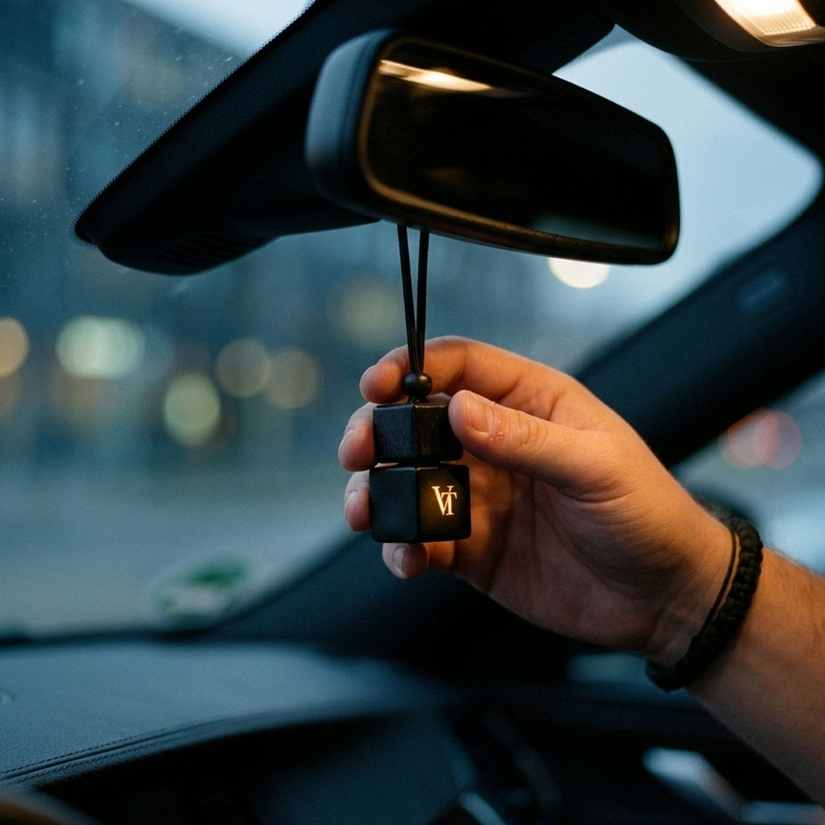 Fahrer hält nachts einen VT Flakon am schwarzen Band vor den Rückspiegel, vor der Windschutzscheibe eine beleuchtete Straße.